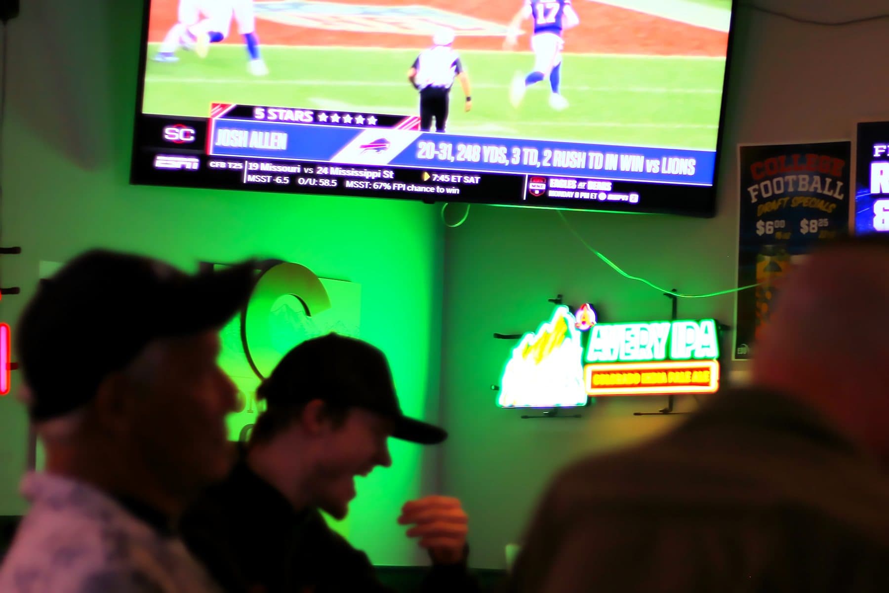 Two regulars laughing at the bar under a football replay on the TV