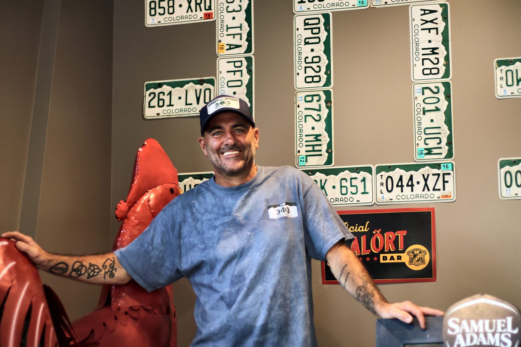 Rick, our manager, smiling in front of the license plate wall that spells 303
